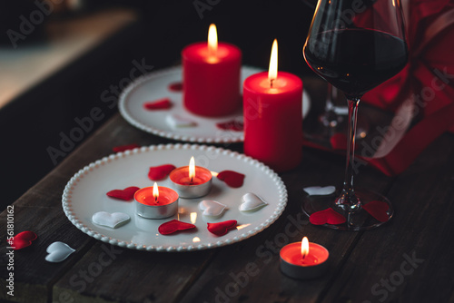 Saint Valentine's Day celebration. Red burning candles, hearts, gift box, postcard on dark wooden background. Happy holiday . Table decor for festive dinner, romantic atmosphere photo