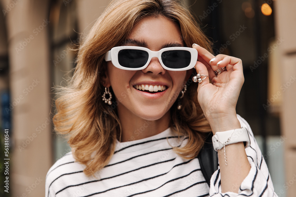 Close up view of caucasian happy woman in sunglasses on the street. Focused on blonde looking with smile to camera. Lifestyle concept Close up view of caucasian happy woman in sunglasses on the street. Focused on blonde looking with smile to camera. Lifestyle concept