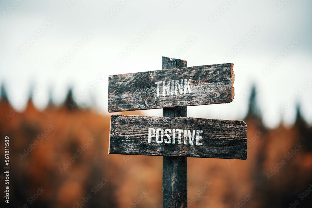 vintage and rustic wooden signpost with the weathered text quote think positive, outdoors in nature. blurred out forest fall colors in the background.