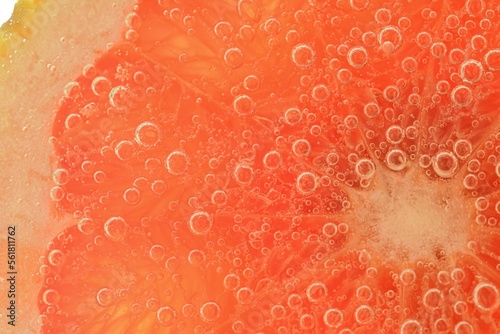 Slice of grapefruit in sparkling water. Grapefruit slice covered by bubbles in carbonated water. Grapefruit slice in water with bubbles