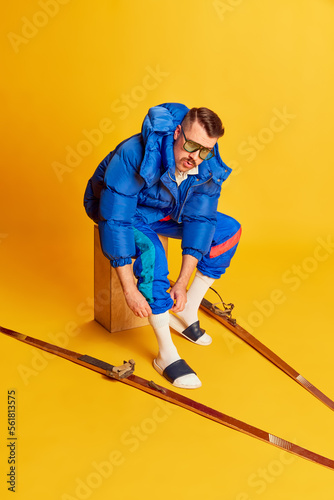 Emotive face. Portrait of handsome man in blue winter jacket posing with skis over bright yellow background. Concept of leisure time, winter sport, hobby