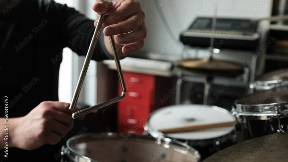 Man hand playing on music triangle beating with metal stick and waiting sound. Musician with traditional instrument in recording studio
