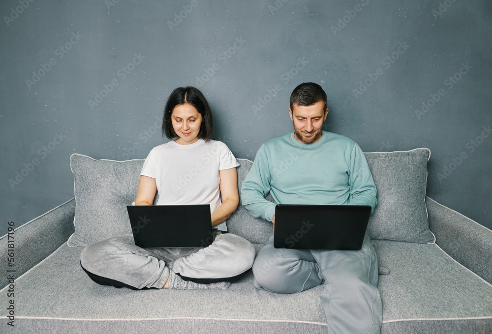 Young couple working on their laptop computer sitting on couch at home Young couple working on their laptop computer sitting on couch at home