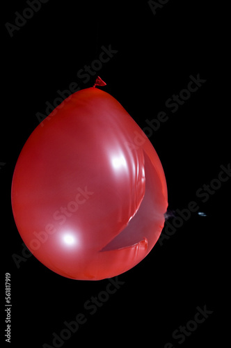 A smoke filled red balloon bursting when shot with an air rifle.  Pellet visible