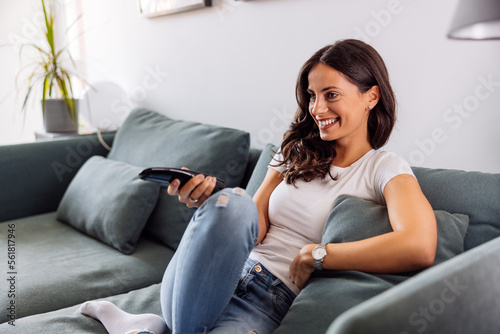 Free Download A smiling young woman sitting on the sofa and watching television. - GFXLoad