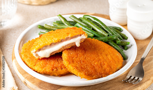 Plate with fried chicken Cordon bleu with melted cheese and ham, in breadcrumbs, green beans and lemon. photo
