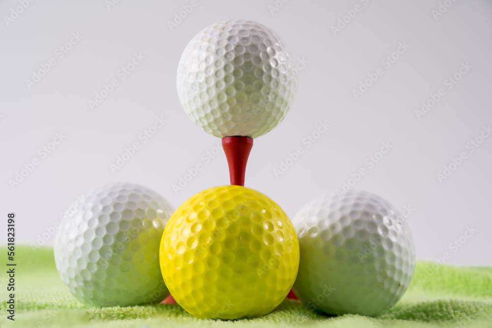 Golf ball on red wooden bamboo tee surrounded by white and yellow balls on a green carpet golf practice mat Golf ball on red wooden bamboo tee surrounded by white and yellow balls on a green carpet golf practice mat
