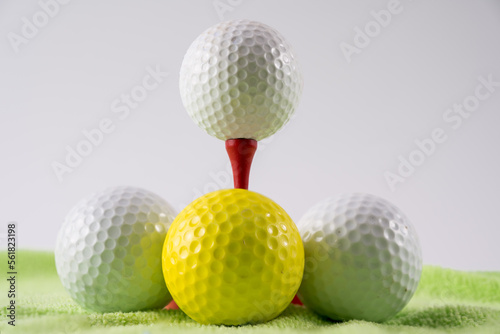 Golf ball on red wooden bamboo tee surrounded by white and yellow balls on a green carpet golf practice mat