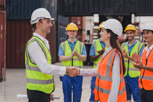 Caucasian engineer wearing safety vest standing by shipping container terminal and shake hand with collaborator. Transportation goods business in the shipping yard. Logistic industrial concept