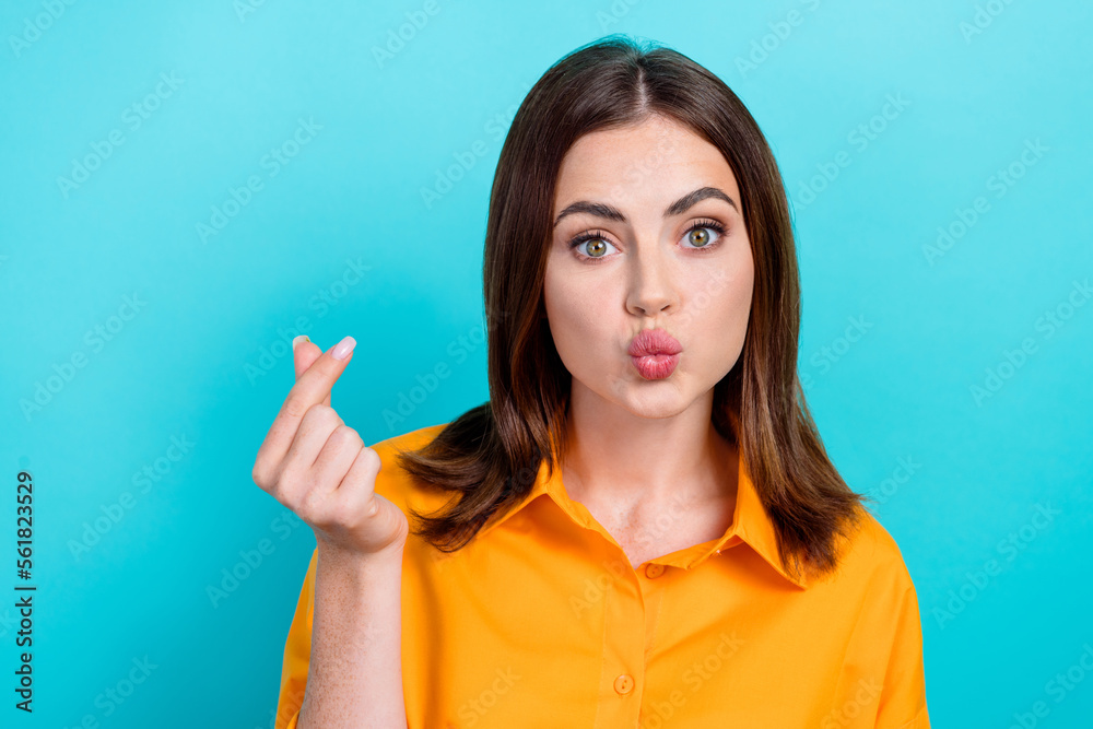 Photo of charming funny lady wear orange shirt sending you kiss showing korean love sign isolated turquoise color background Photo of charming funny lady wear orange shirt sending you kiss showing korean love sign isolated turquoise color background