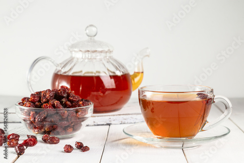 A cup of brewed rosehip medicinal plants herbal tea on a white wooden vintage table with dried rosehips