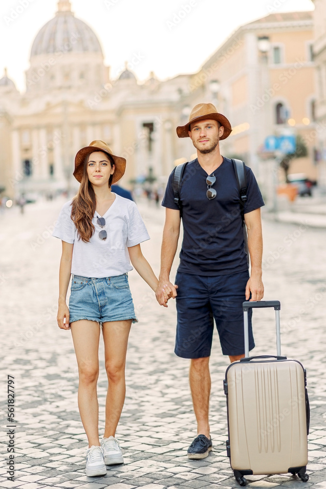 Happy young couple of travellers with hats and a suitcase hugging in the city and enjoying romance. Lovers smiling and have fun together. tourism. cheerful couple in casual clothes traveling the world