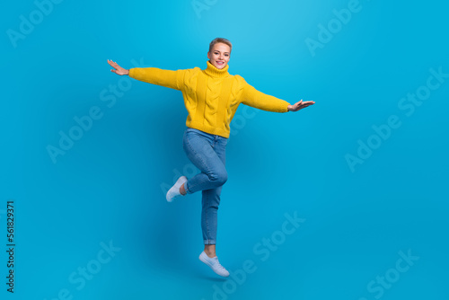 Full length size photo of excited energetic jumping air flying young woman wear knit pullover hands wings traveler isolated on blue color background