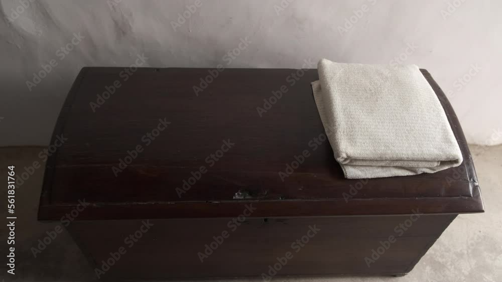 Manos cogiendo toalla blanca doblada sobre un baúl de madera antiguo.