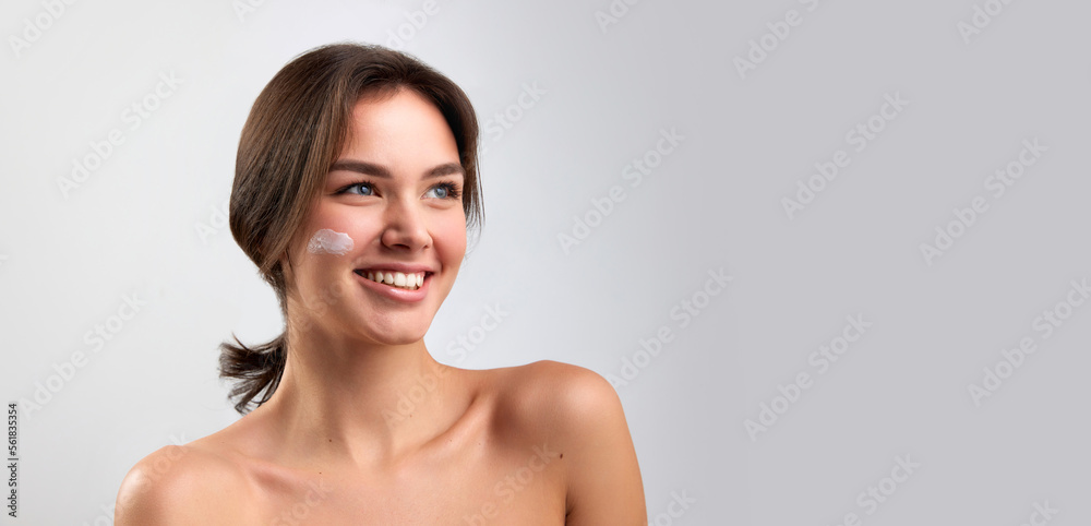 Banner with portrait of happy beautiful woman with bared shoulders applying face cosmetics products and looking with delighted facial expression isolated over light background Banner with portrait of happy beautiful woman with bared shoulders applying face cosmetics products and looking with delighted facial expression isolated over light background
