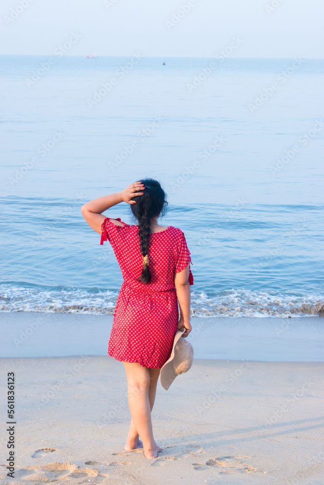 Attractive and Happy woman or lady in red dress enjoys her tropical vacation on beach. Sand and blue water of Sea . selective focus on subject.
