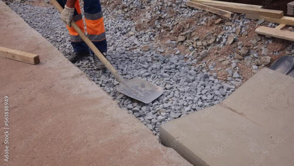Worker is rammed, leveled gravel before laying concrete blocks for draining on the side of the