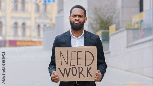 Sad frustrated hopless fired African American man ethnic upset guy worker in city holding poster need work help searching job offer jobless crisis unemployment business lost bankrupt loosing career photo