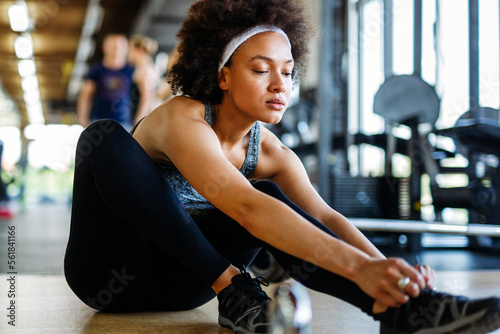 Young sporty black woman tying shoes while sitting on floor in gym.