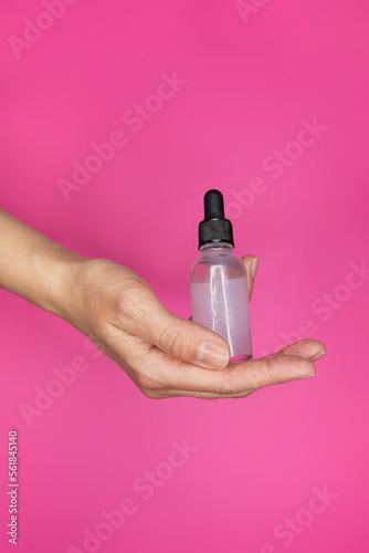 Female hands with pink serum in bottles on pink background