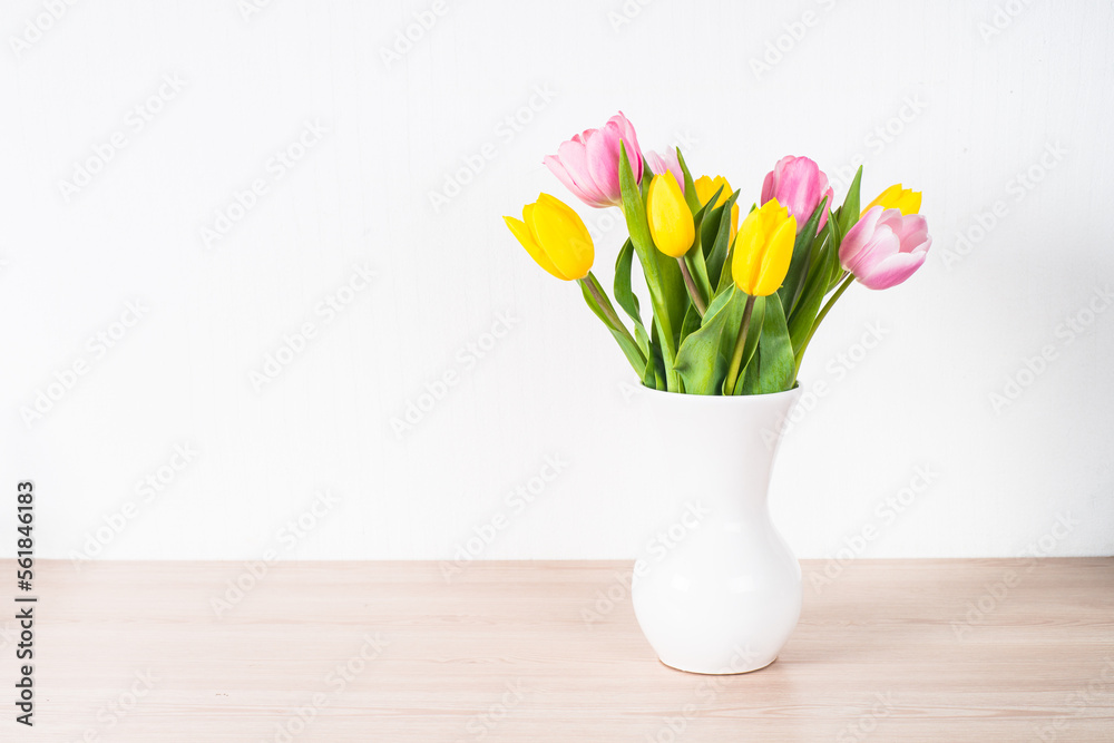 Tulips flower bouquet in white ceramic vase at light background.