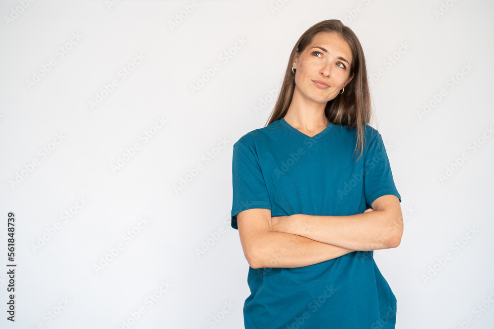 Unsure Caucasian woman with crossed arms. Portrait of pensive young female model with brown hair in blue T-shirt looking away at ads, considering special offer. Advertisement, doubt concept Unsure Caucasian woman with crossed arms. Portrait of pensive young female model with brown hair in blue T-shirt looking away at ads, considering special offer. Advertisement, doubt concept