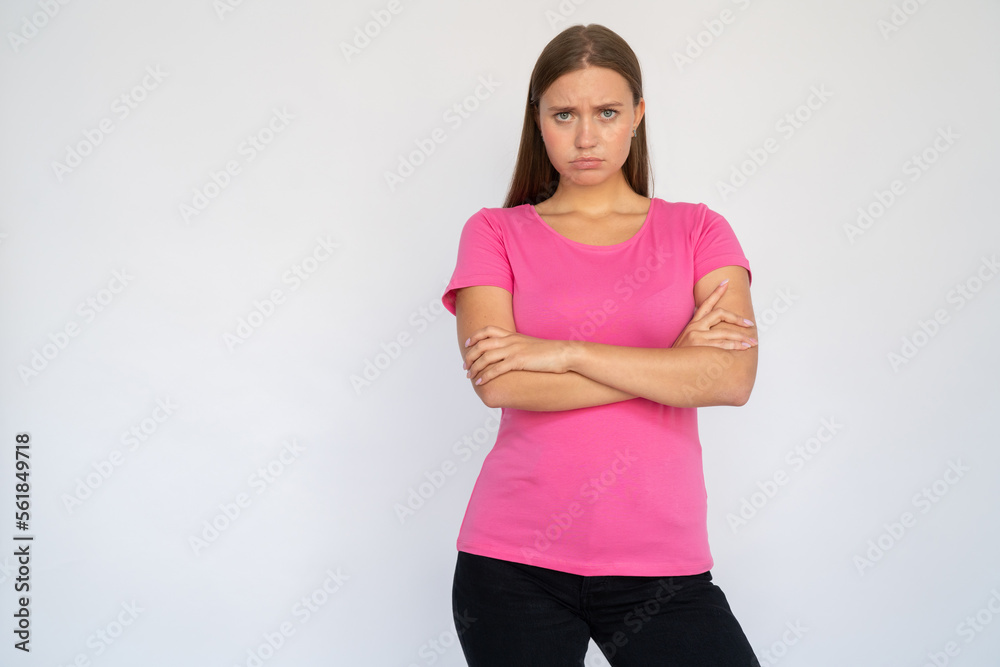 Sad young woman crossing arms. Portrait of upset Caucasian female model with brown hair in pink T-shirt looking at camera, frowning, pouting lips. Offense, sadness concept Sad young woman crossing arms. Portrait of upset Caucasian female model with brown hair in pink T-shirt looking at camera, frowning, pouting lips. Offense, sadness concept