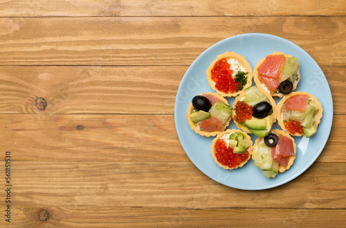 Tartlets with salmon and caviar on wooden background, top view