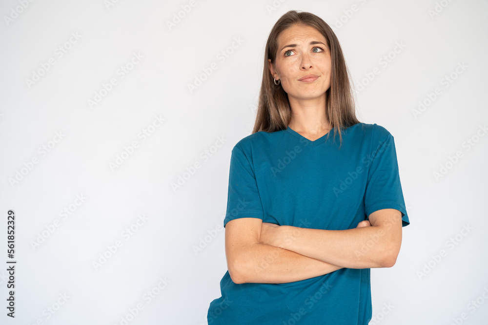 Uncertain Caucasian woman with crossed arms. Portrait of unsure young female model with brown hair in blue T-shirt looking up, considering special offer. Advertisement, doubt concept Uncertain Caucasian woman with crossed arms. Portrait of unsure young female model with brown hair in blue T-shirt looking up, considering special offer. Advertisement, doubt concept