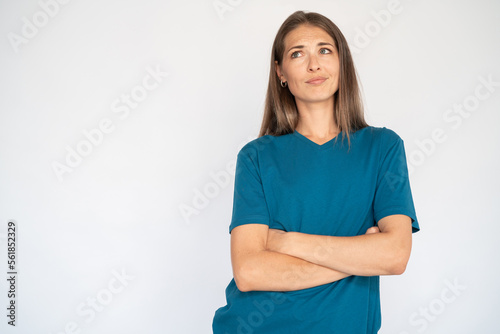 Uncertain Caucasian woman with crossed arms. Portrait of unsure young female model with brown hair in blue T-shirt looking up, considering special offer. Advertisement, doubt concept