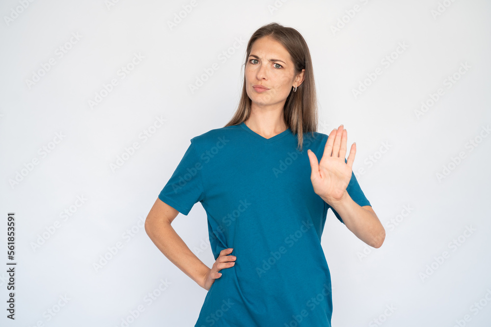 Strict Caucasian woman showing stop sign. Portrait of displeased young female model with brown hair in blue T-shirt looking at camera with open palm, frowning. Restriction, refusal concept Strict Caucasian woman showing stop sign. Portrait of displeased young female model with brown hair in blue T-shirt looking at camera with open palm, frowning. Restriction, refusal concept