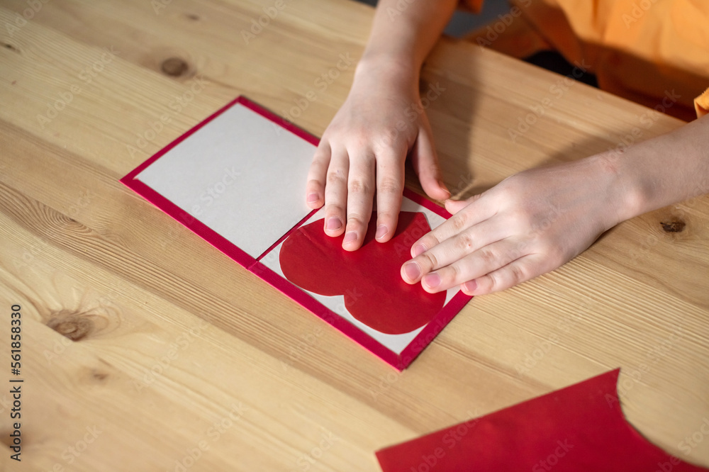 Children's hands make a postcard with a heart of colored paper