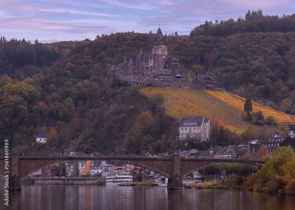 A beautiful autumn view of the city of Cochem on the Moselle River with its old bridge and castle atop a hill full of colorful vines.