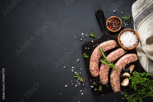 Bratwurst or sausages on cutting board with rosemary at black table. Ready for cooking. Top view with copy space. photo
