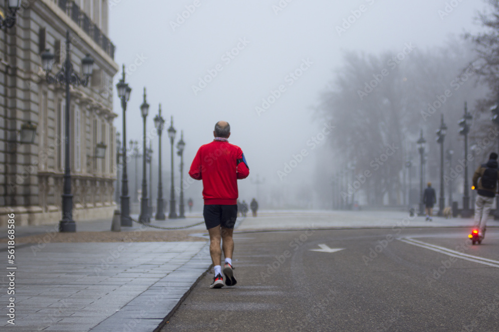 Back view of a man with red t-shirt running in a foggy street 