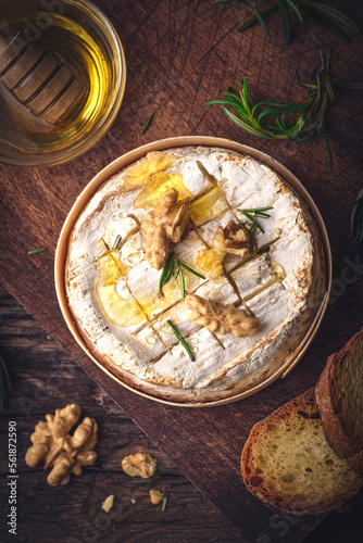 French cheese Camembert baked in a wooden box served with honey, aromatic herbs and nuts. Taste of France, rustic style, top view
