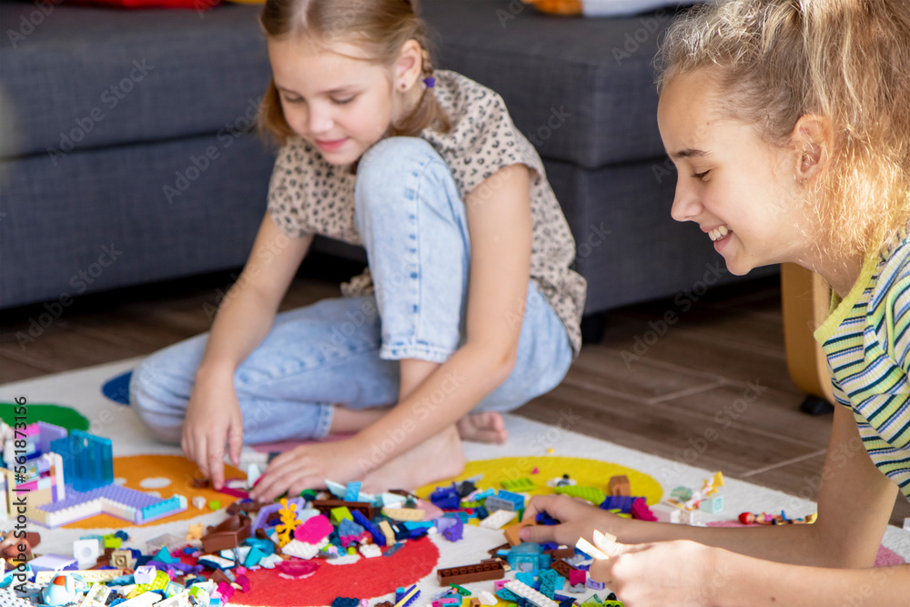 Fototapeta premium Two little girls sisters play with colorful toy blocks at home in the living room. Educational games for children. Mess in the playroom.