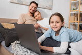 cheerful kid using laptop near happy parents on blurred background.
