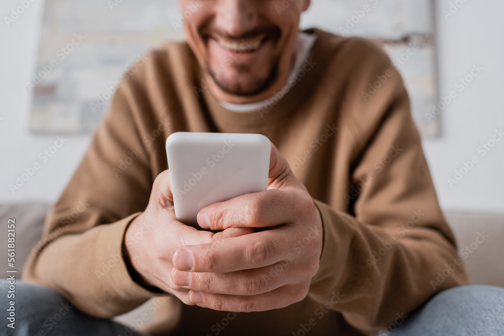 cropped view of happy man in beige jumper using smartphone at home. cropped view of happy man in beige jumper using smartphone at home.