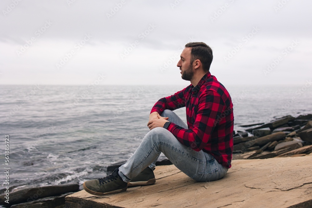 A young man in a red plaid shirt walks in nature near the sea. Beautiful view.