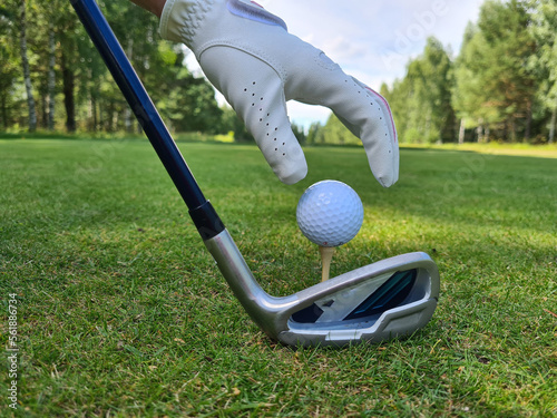 Hand putting golf ball on tee with club in golf course