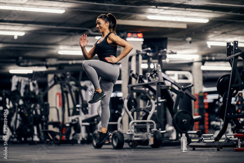 A fit sportswoman is doing cardio exercises and jumping in place in a gym.