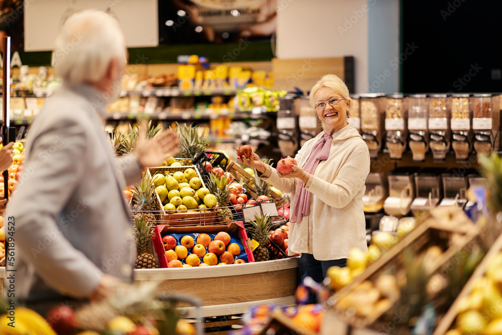 A cheerful old couple is choosing fresh fruits and buying it at the supermarket.