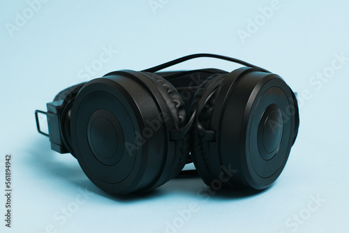 New black headphones with a wire on a light blue paper background