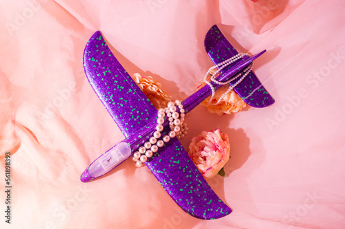Purple children's plane lies among the flowers surrounded by beads and dramatic shadows.
