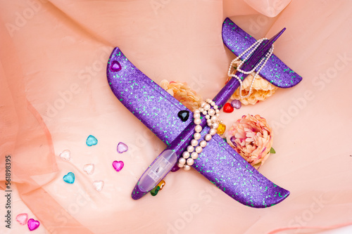 Purple children's plane lies among the flowers surrounded by beads and transparent colored hearts