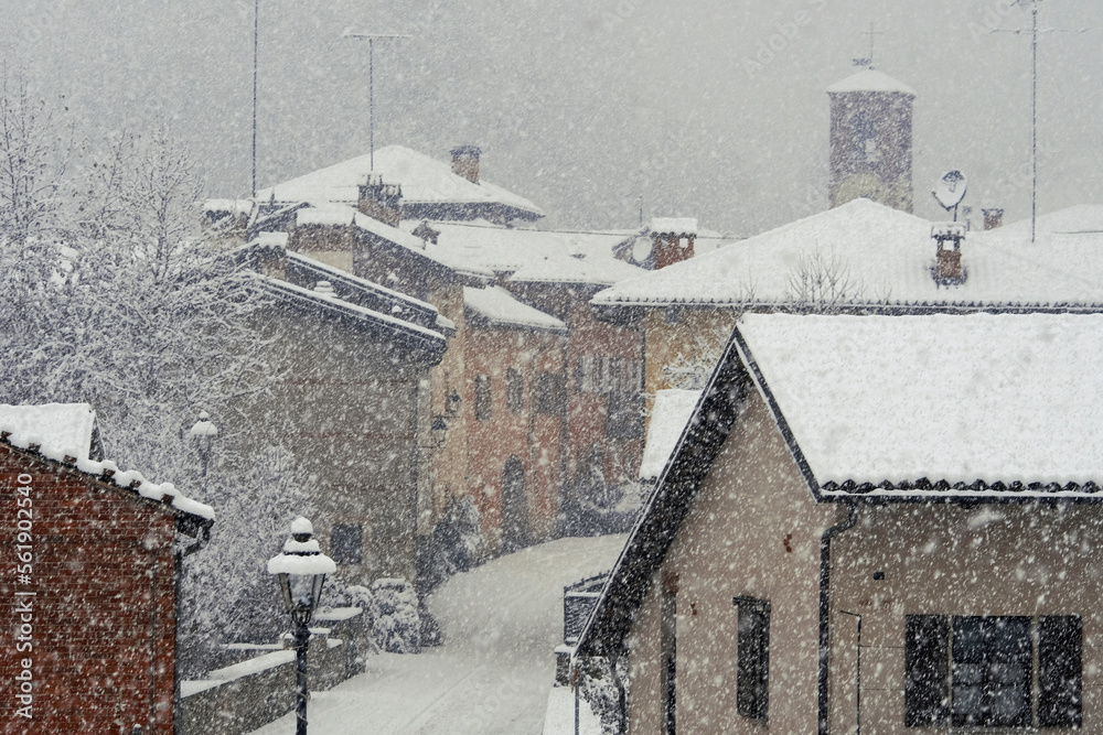 Snowfall in a typical rural italian country town with the houses and bell tower facing the central street. Italy, Piedmont.
