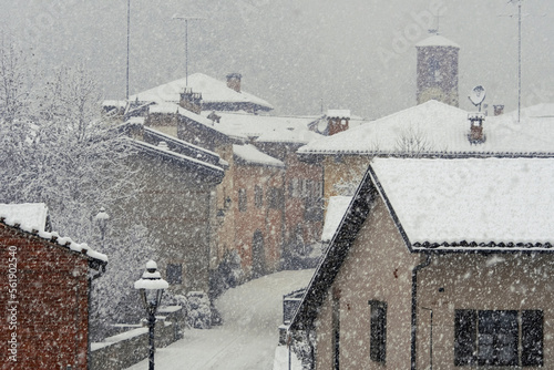 Obraz na płótnie Snowfall in a typical rural italian country town with the houses and bell tower facing the central street. Italy, Piedmont. w salonie