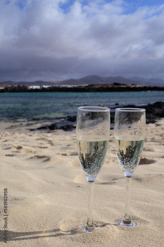 Two glasses of white champagne or cava sparkling wine served on white sandy tropical beach and blue ocean, romantic vacation, winter sun on Fuerteventura, Canary, Spain Two glasses of white champagne or cava sparkling wine served on white sandy tropical beach and blue ocean, romantic vacation, winter sun on Fuerteventura, Canary, Spain