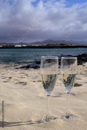 Two glasses of white champagne or cava sparkling wine served on white sandy tropical beach and blue ocean  romantic vacation  winter sun on Fuerteventura  Canary  Spain